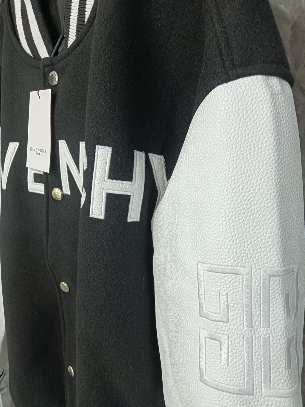 Givenchy varsity jacket close-up: black body with white textured sleeves and logo