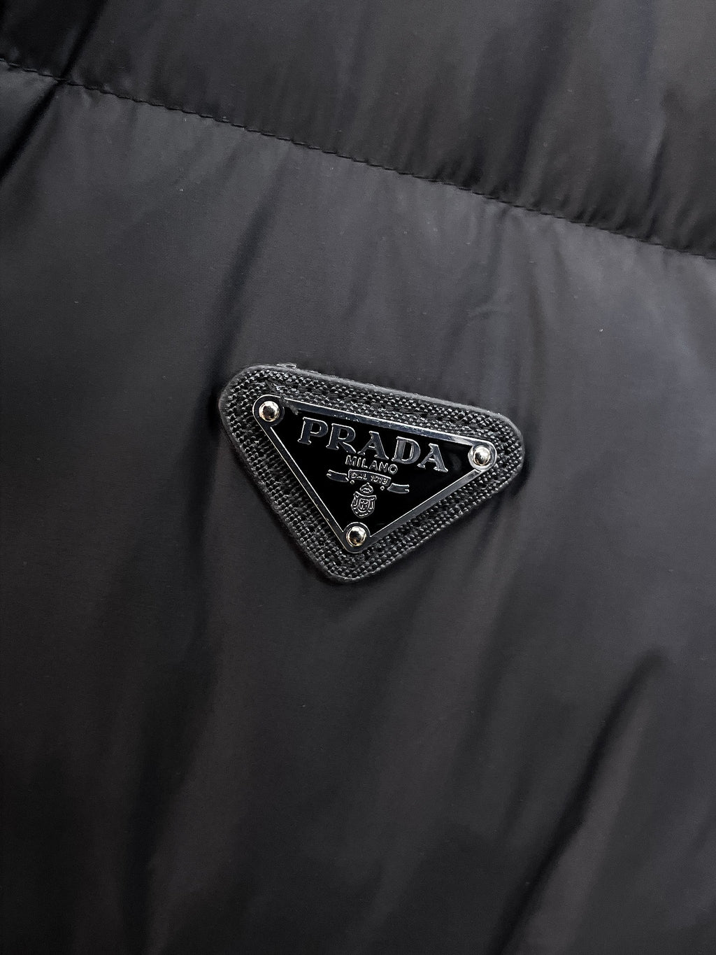 Close-up of embroidered triangular logo patch on dark puffer vest