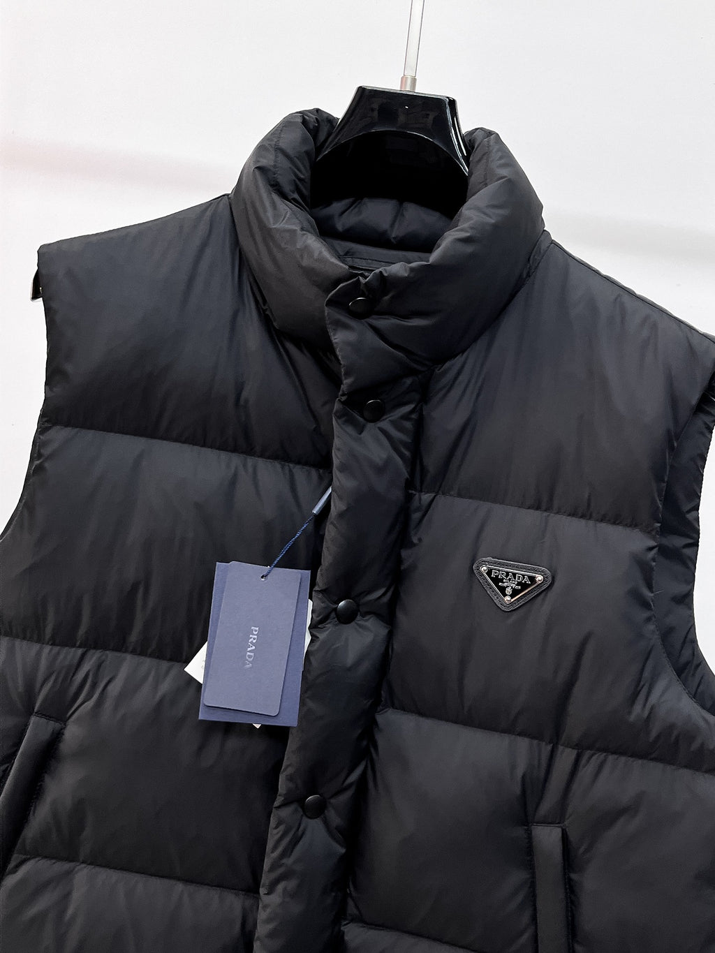 Close-up of dark hooded puffer vest with front button placket and logo triangle