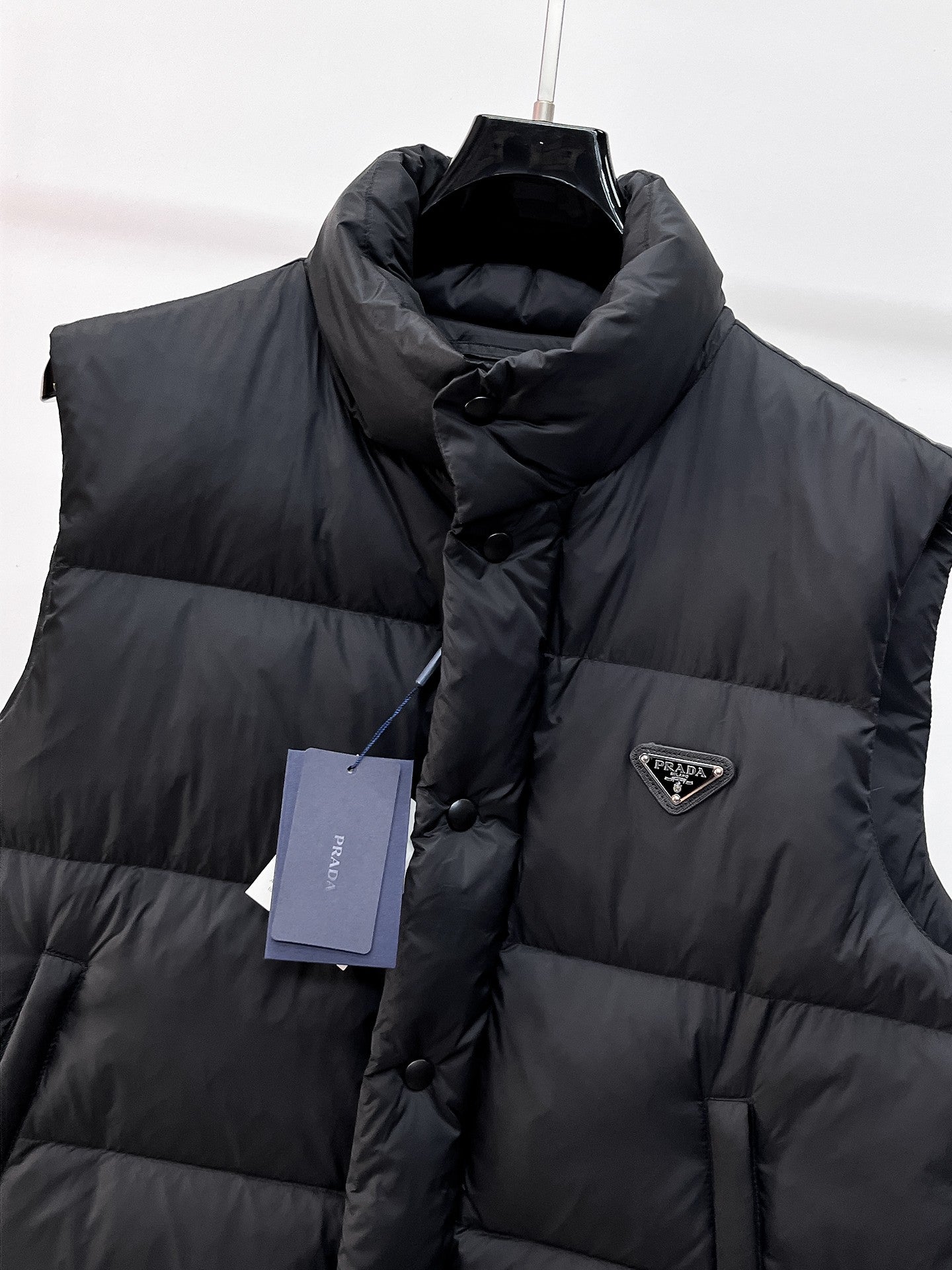 Close-up of dark hooded puffer vest with front button placket and logo triangle