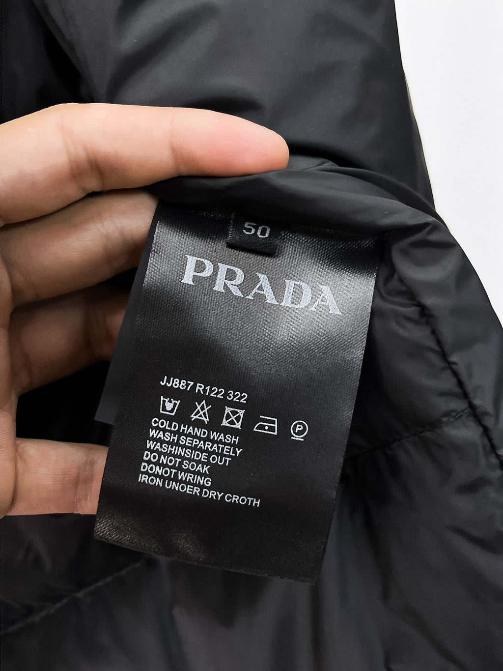 Care label on dark puffer vest with PRADA branding and washing instructions