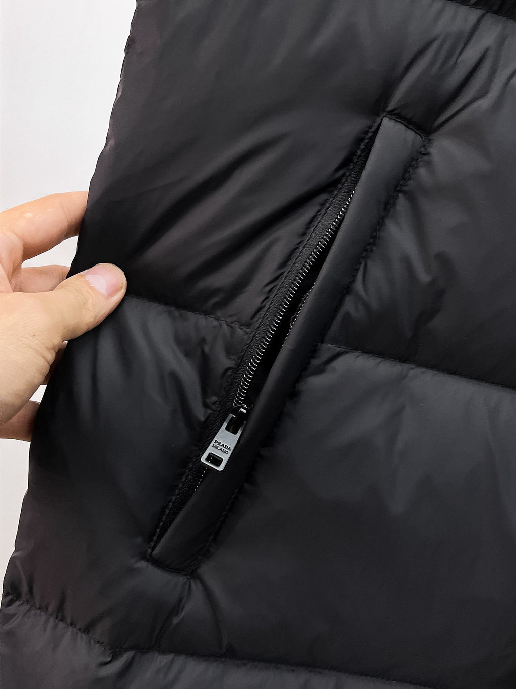 Close-up of dark puffer vest side with zipper placket and stitched seam