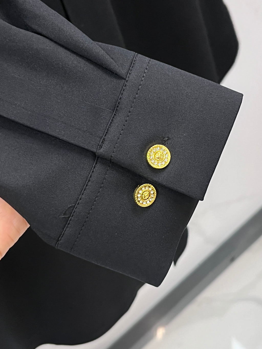 Black shirt cuff with gold buttons and stitched sleeve edge detail