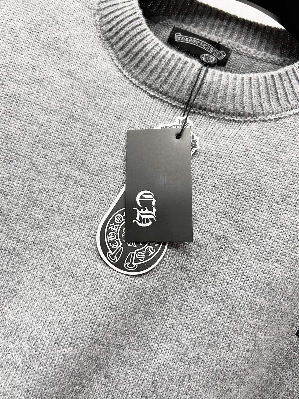 Gray knit sweater neckline with hanging brand tag at collar