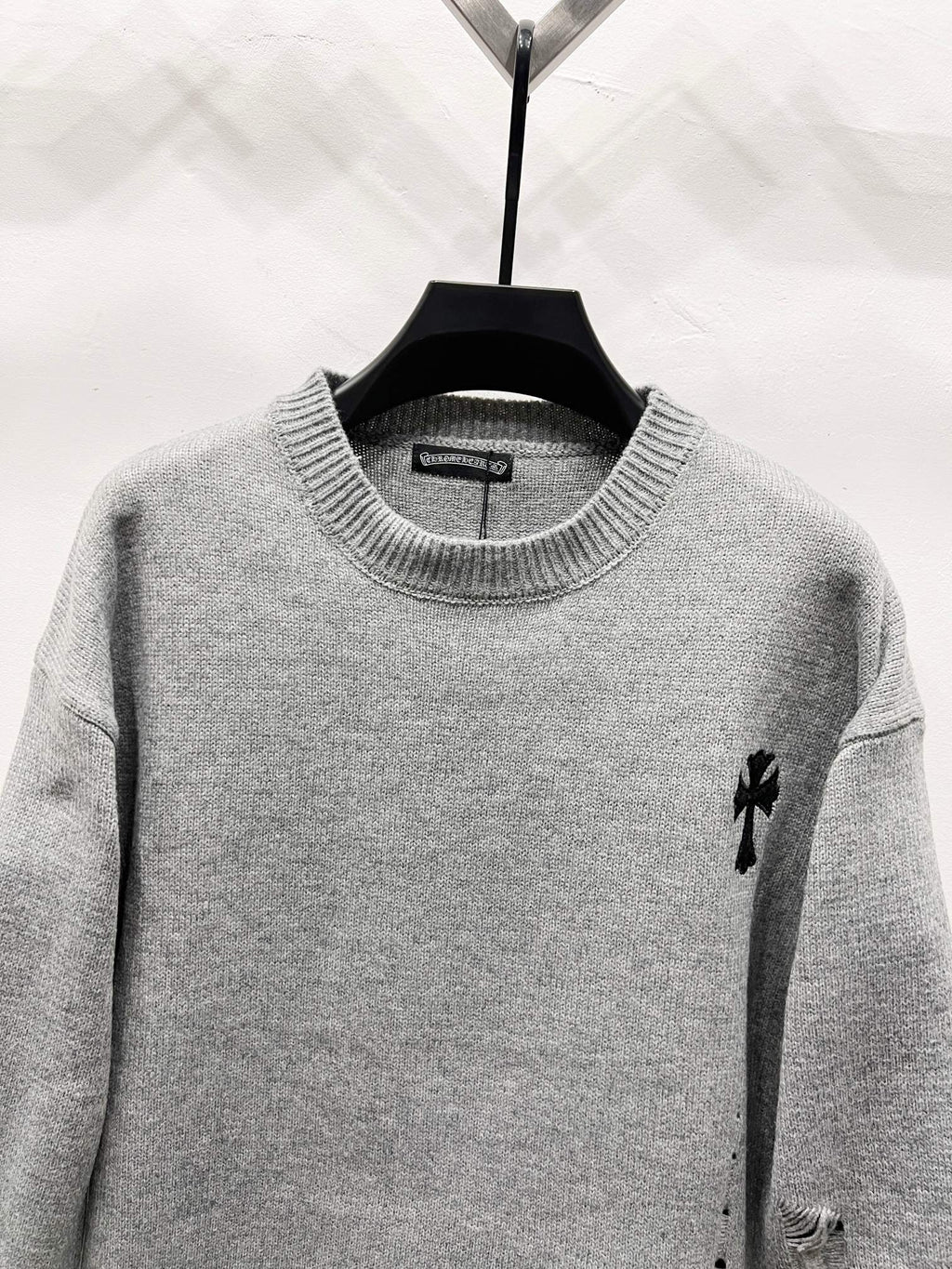 Gray crewneck knit sweater with small black emblem on right shoulder