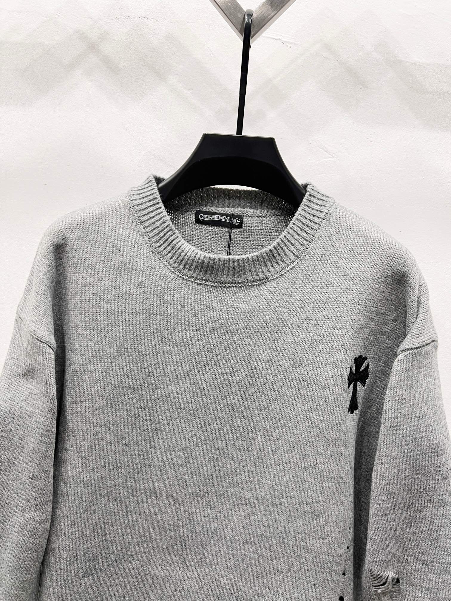 Gray crewneck knit sweater with small black emblem on right shoulder