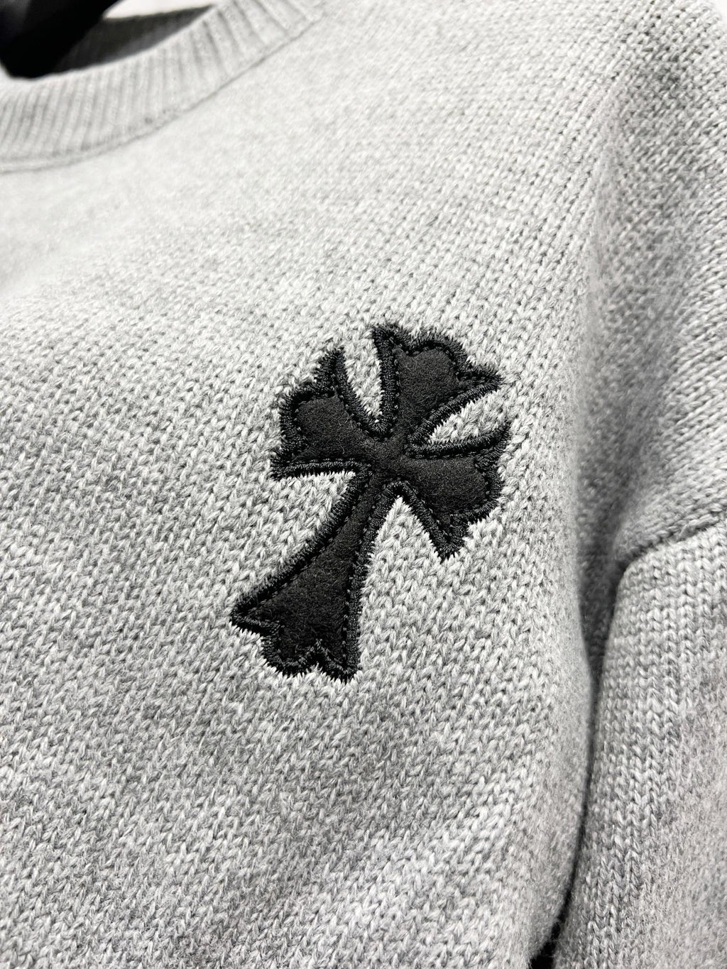 Gray knit sweater close-up of black cross-like emblem on chest