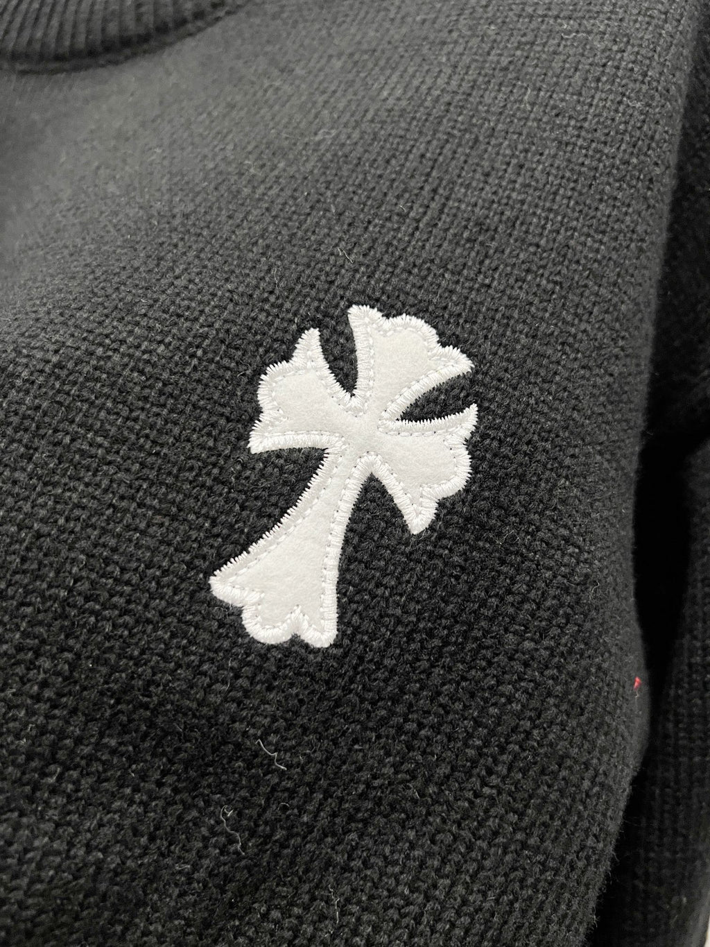Black knit sweater with large white cross-flower applique on the front