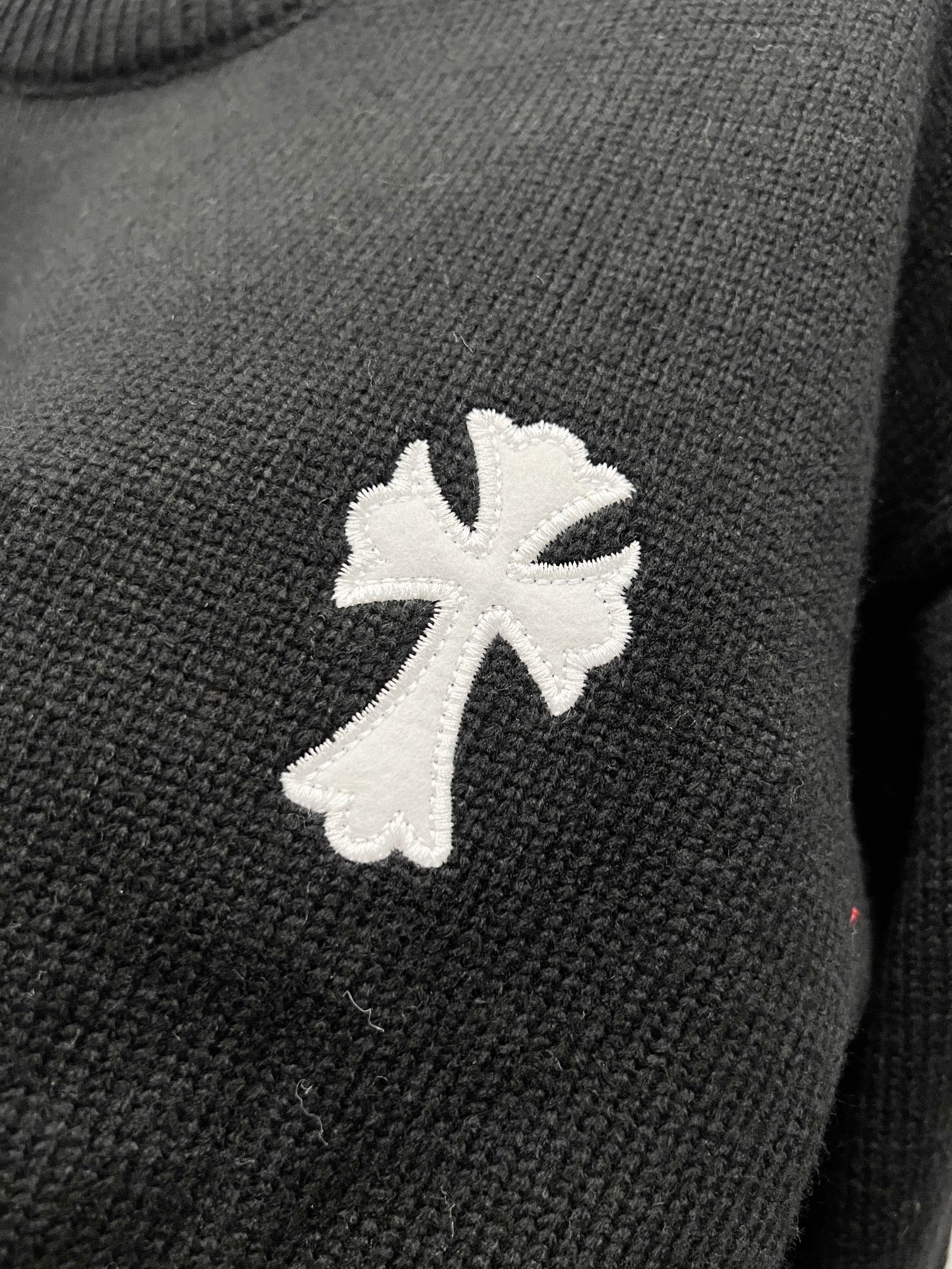 Black knit sweater with large white cross-flower applique on the front