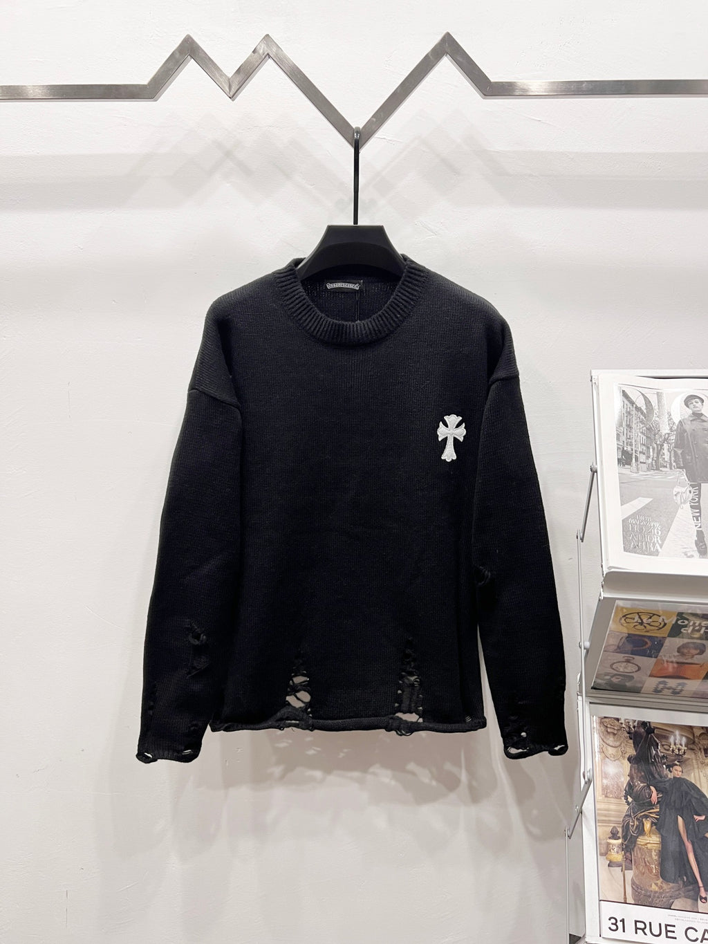 Black knit long-sleeve sweater with small white crest emblem on left chest