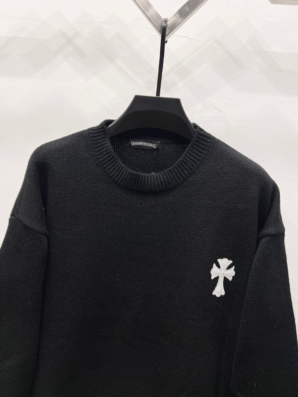 Black knit crewneck sweater with ribbed collar and small white crest patch on sleeve