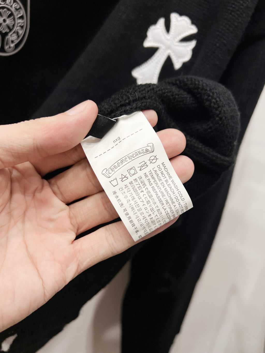 Black knit sweater with white care label tag held near neckline by hand