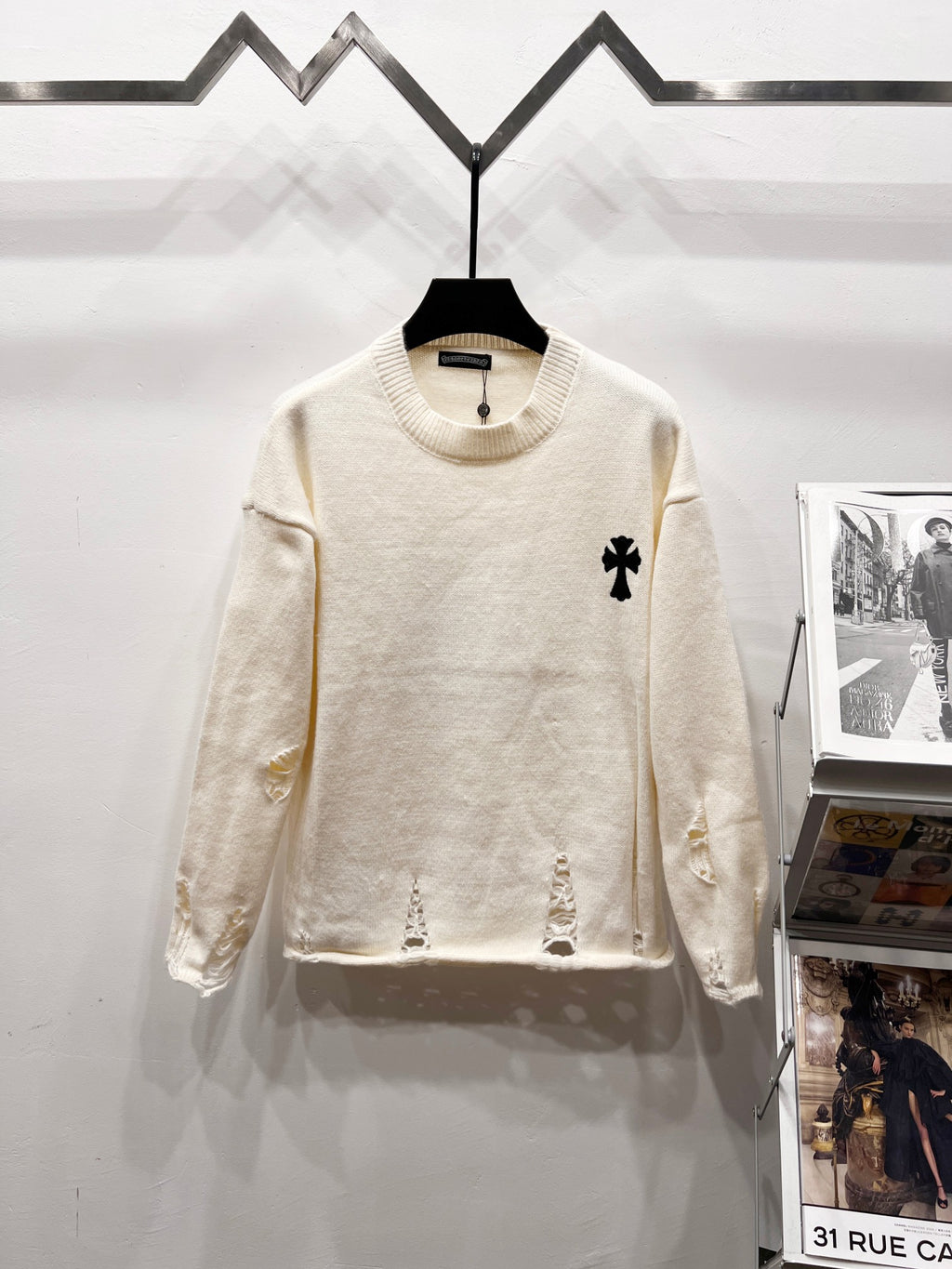Cream long-sleeve knit sweater with ribbed crew neck and small black clover logo on chest