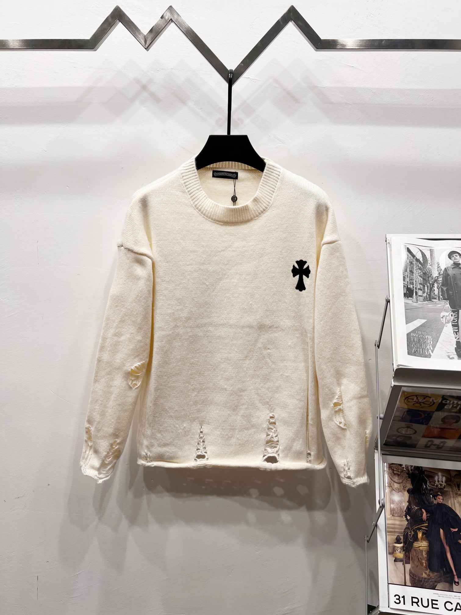 Cream long-sleeve knit sweater with ribbed crew neck and small black clover logo on chest