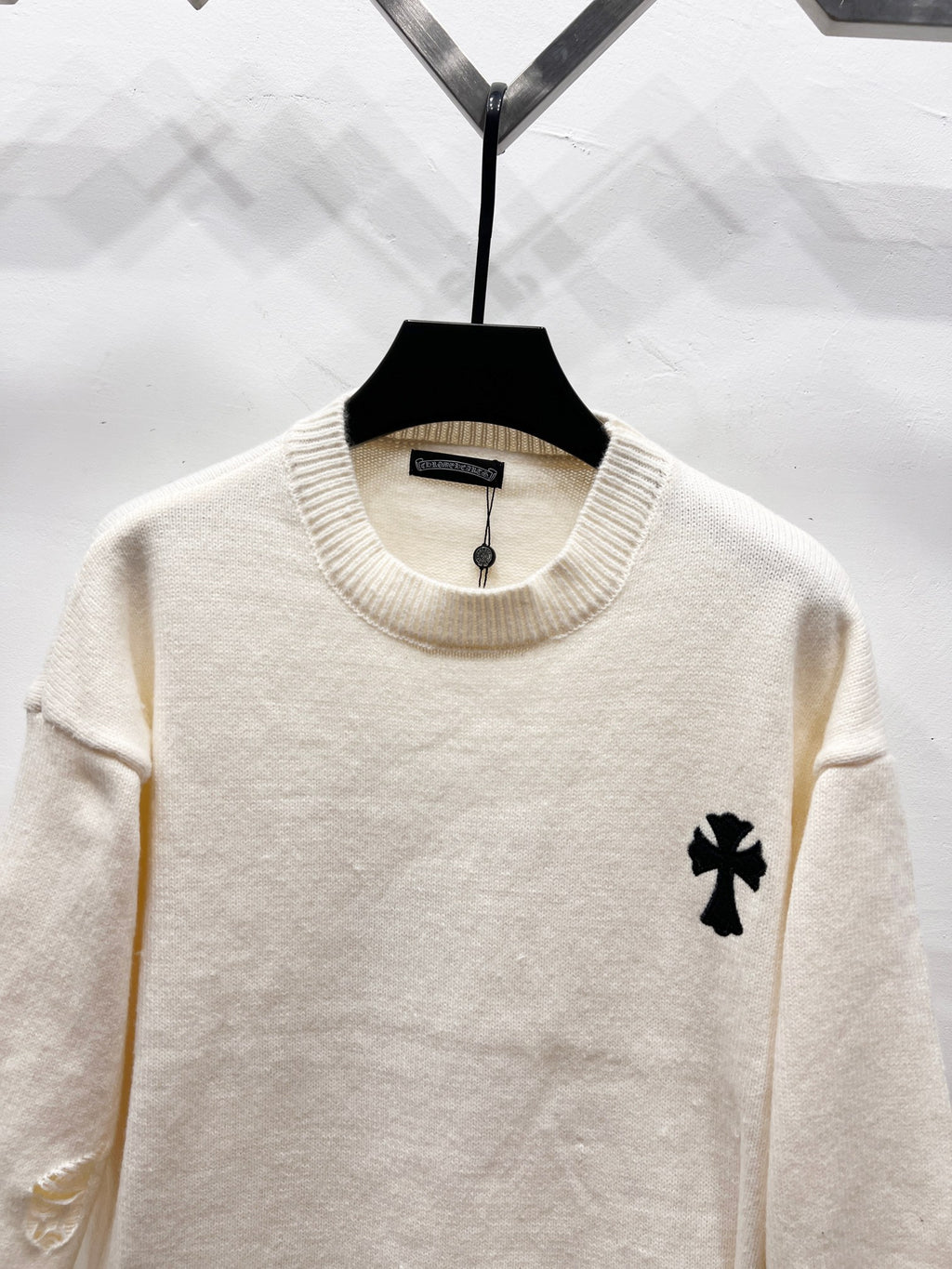 Cream long-sleeve sweater with ribbed crew neck and small black clover patch on chest