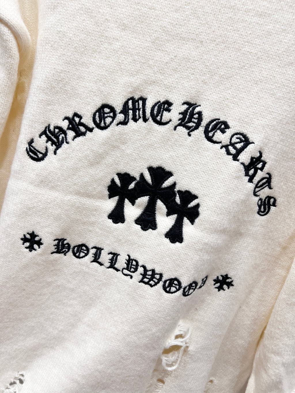 Cream knit sweater with arched black graphic text and three clover emblems on chest