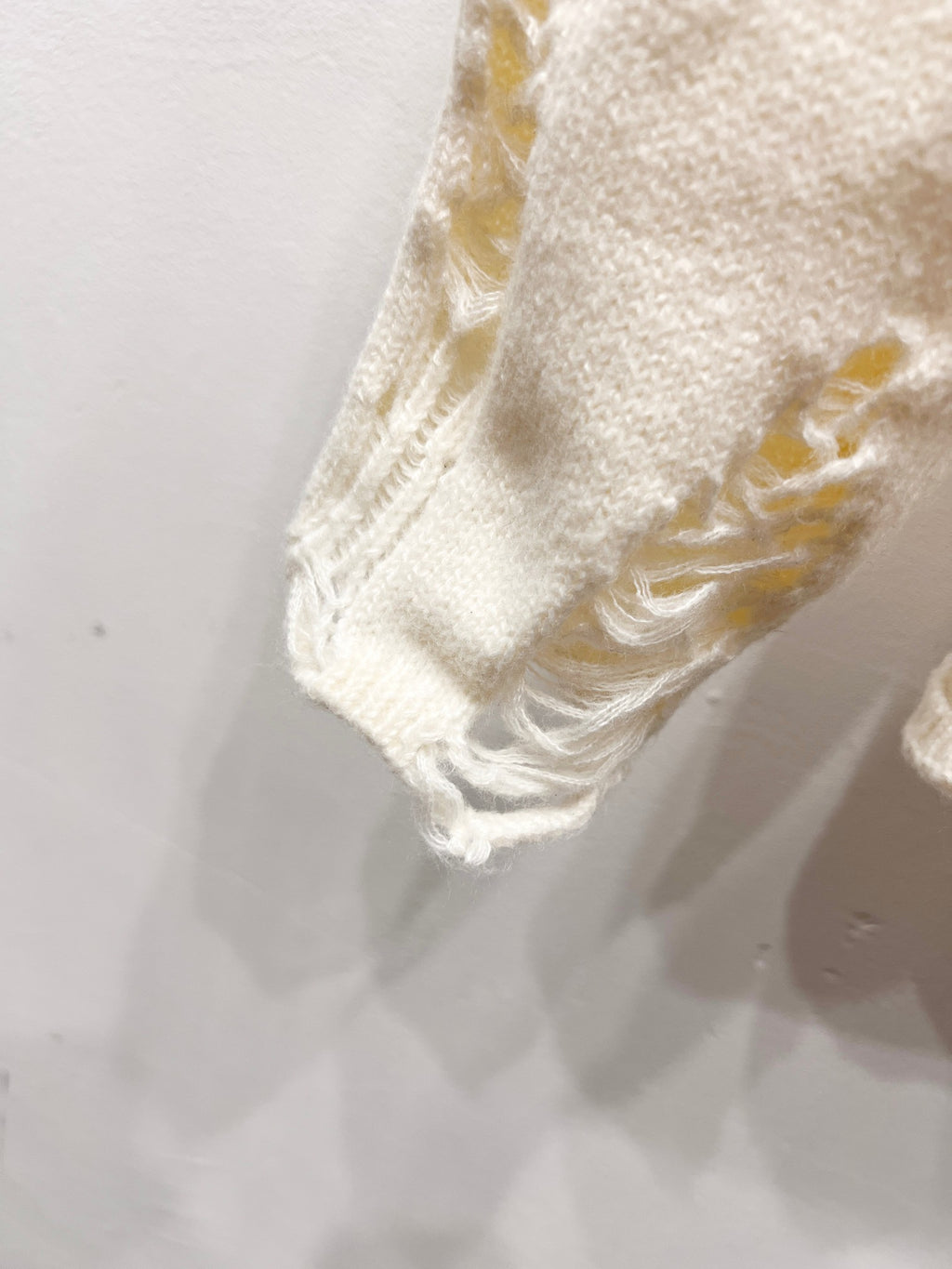 Cream knit sweater sleeve hem with distressed, frayed stitching detail