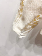 Cream knit sweater sleeve hem with distressed, frayed stitching detail