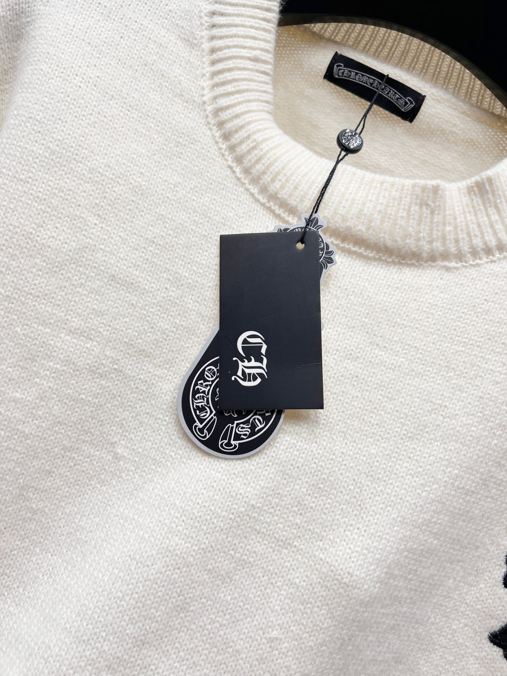 Cream knit sweater neckline with ribbed collar and hanging brand tag
