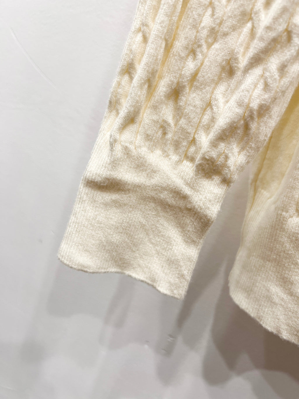 Cream knit cardigan sleeve and hem with textured cable knit pattern