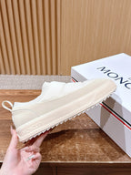 Moncler white slip-on sneaker being held, showing side lettering and thick sole