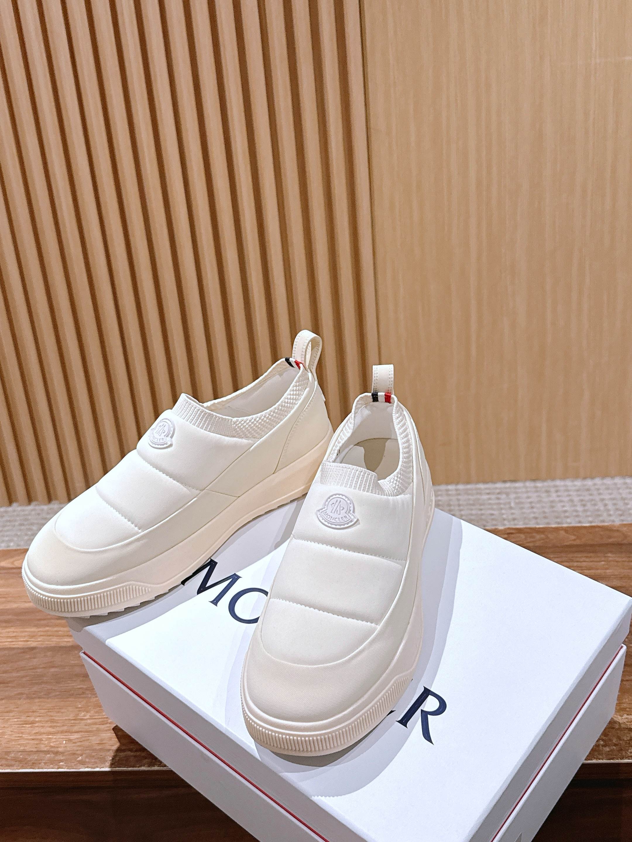 Moncler white slip-on sneakers on a white shoebox, front and side views