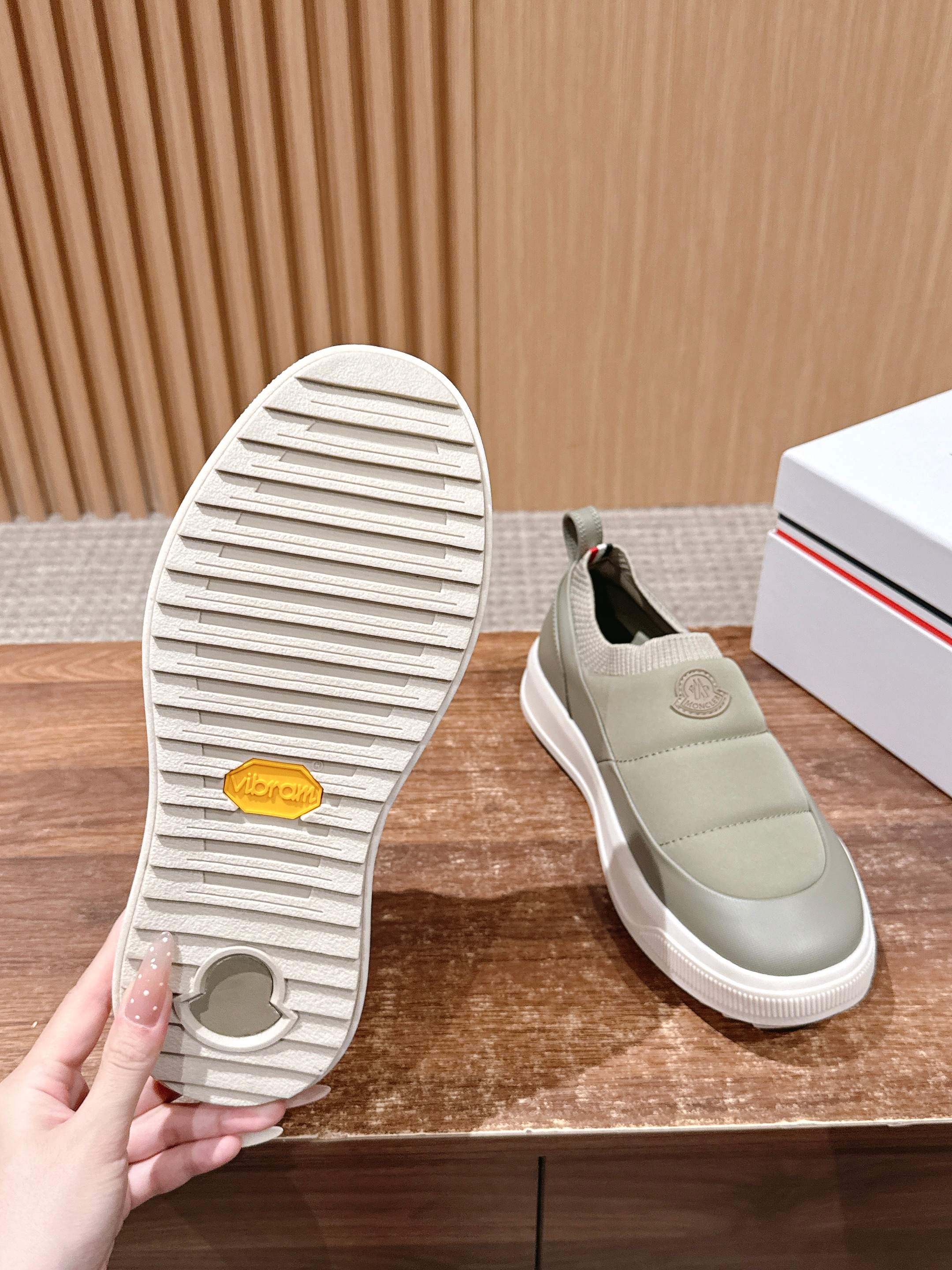 Moncler light beige slip-on sneaker with treaded outsole held next to shoe