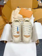 Pair of cream low-top sneakers with white laces, tan accents, and blue logo detail