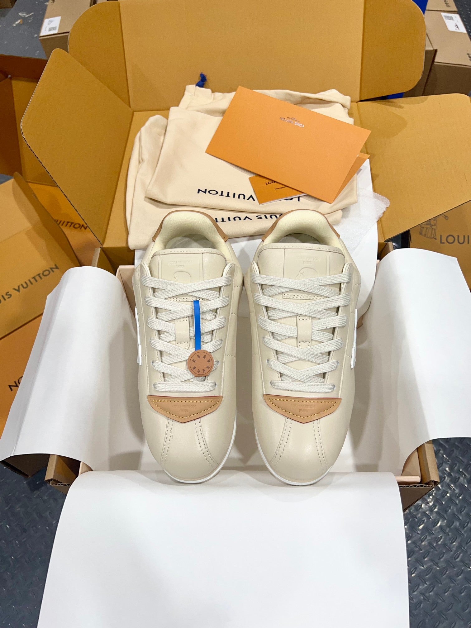 Pair of cream low-top sneakers with white laces, tan accents, and blue logo detail