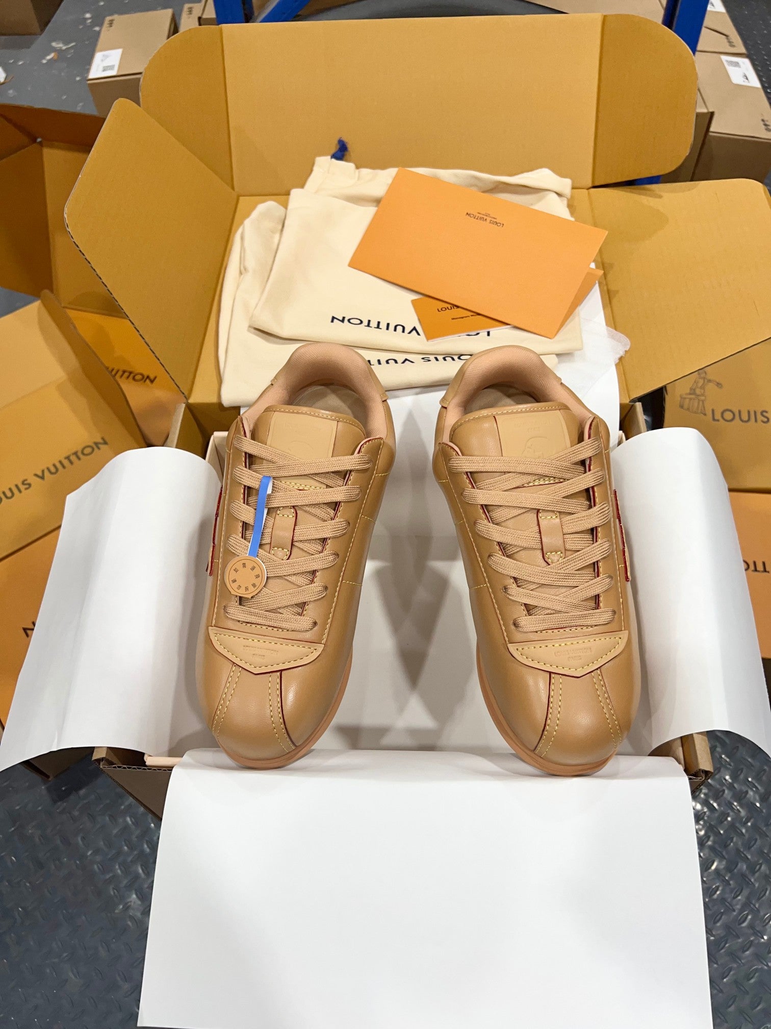 Tan lace-up low-top sneakers, front view with logo patch on tongue