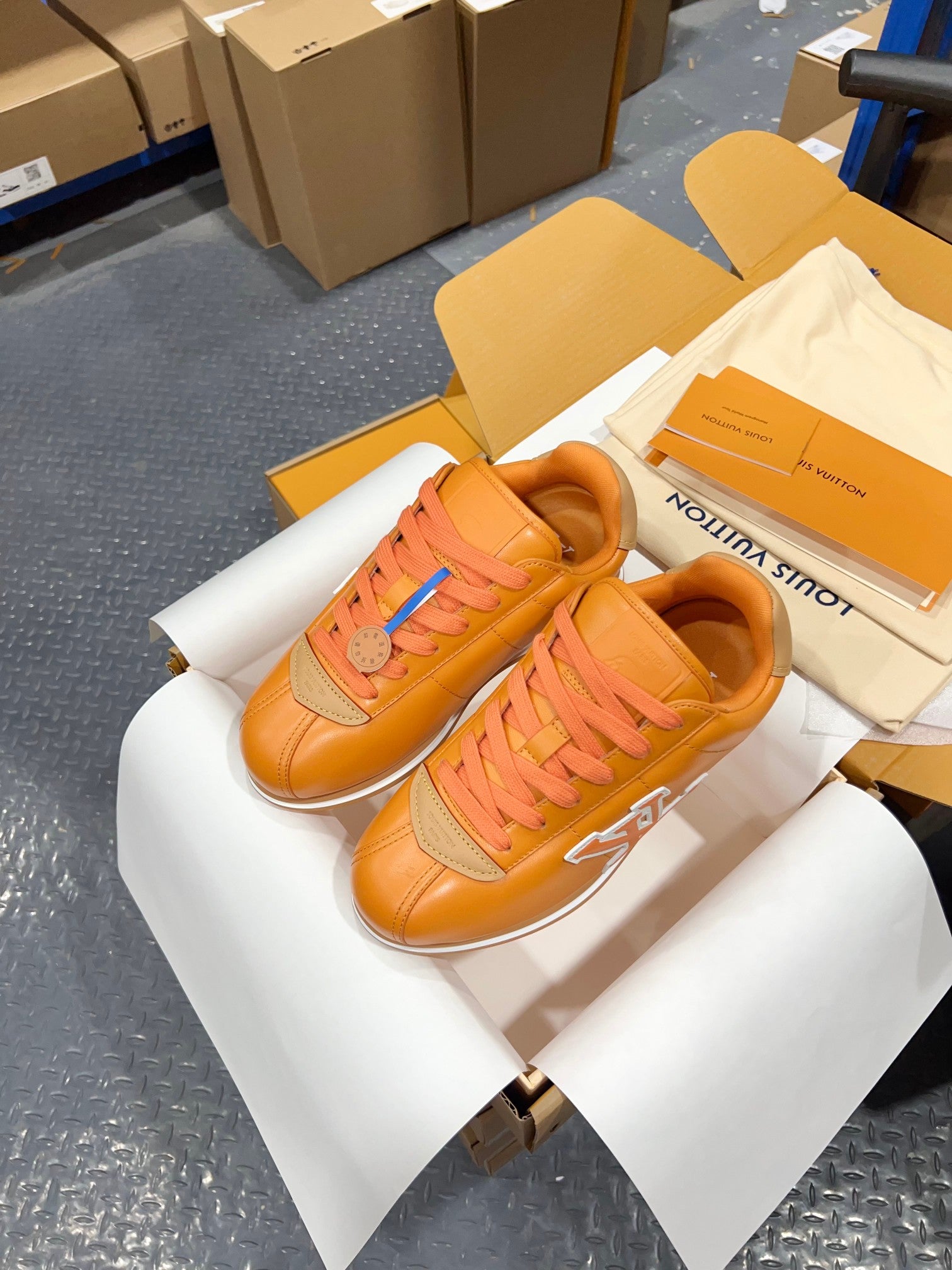 Louis Vuitton unisex sneakers orange leather with LV emblem, side view on white boxes