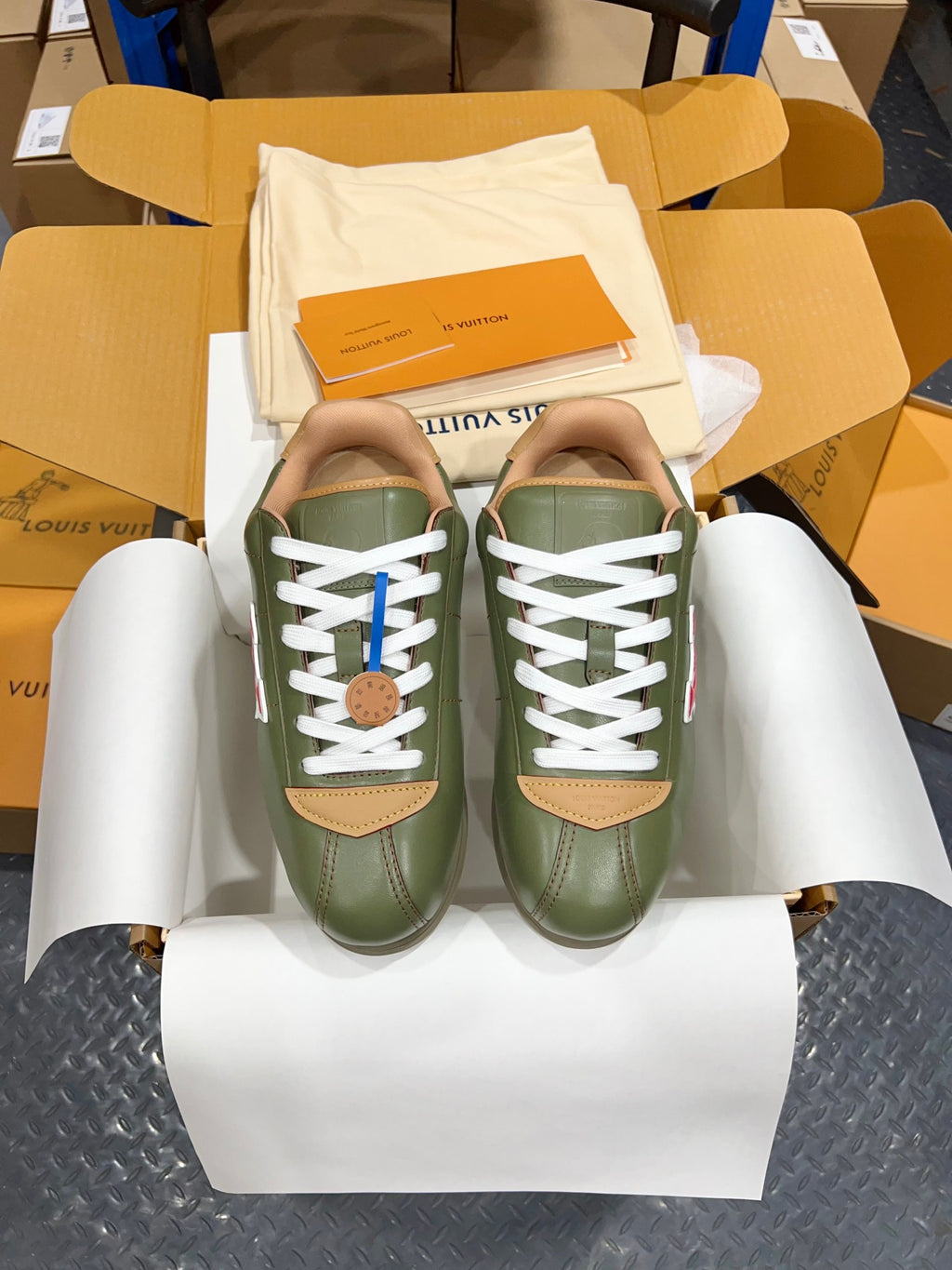Green leather sneakers with white laces and tan logo patches in shoebox