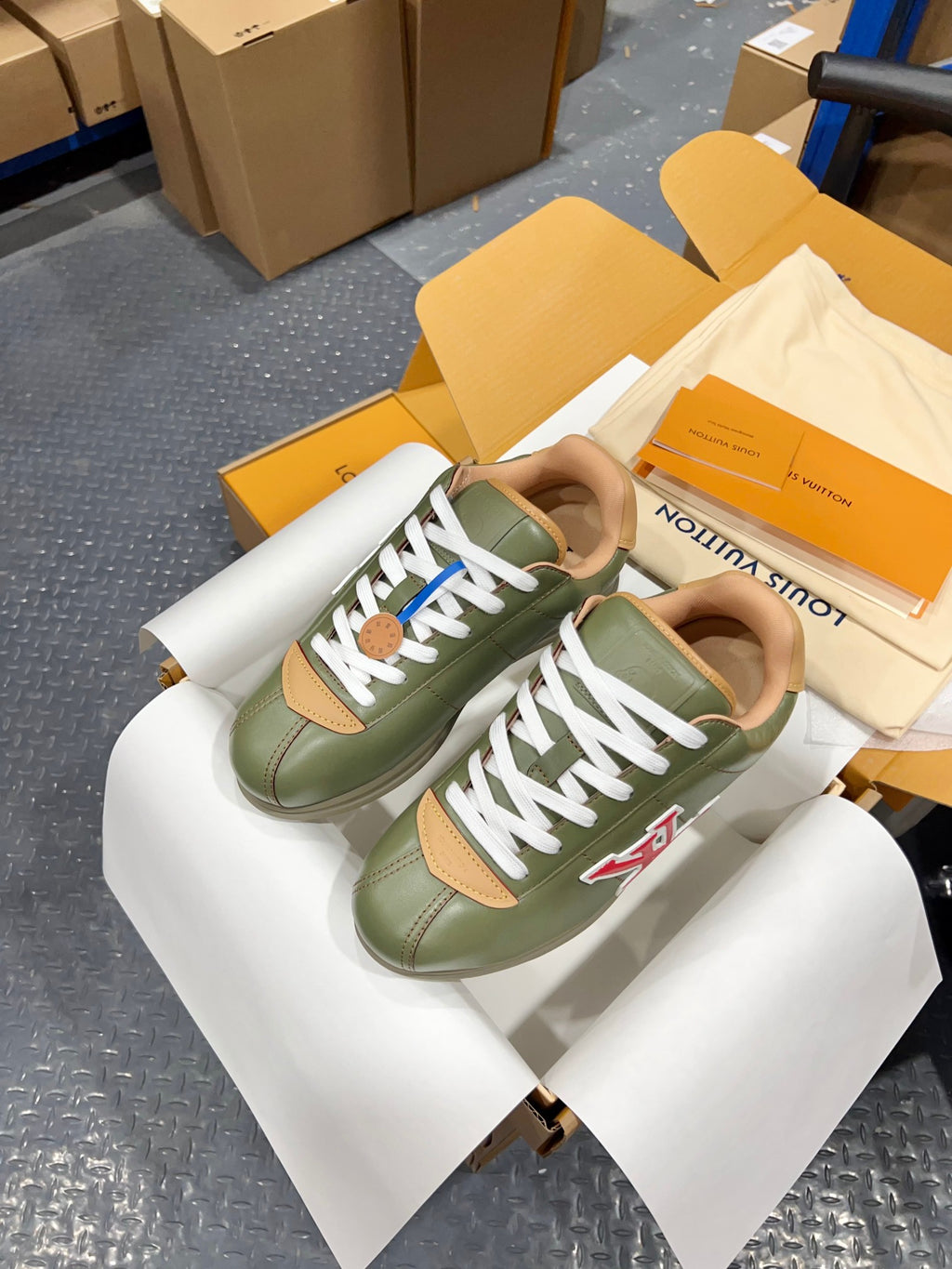 Green leather sneakers on shoe box with white laces and LV side logo