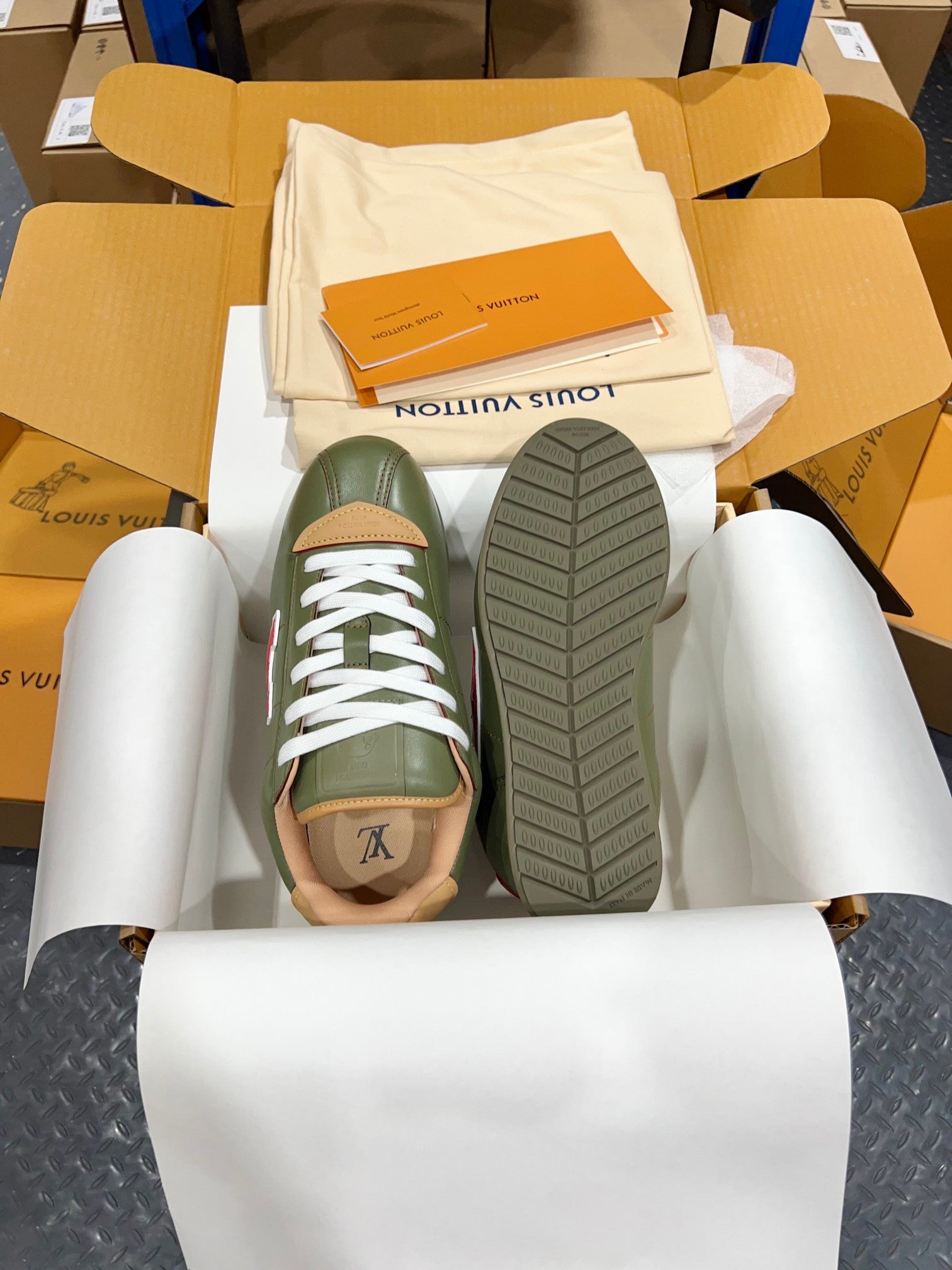 Green leather sneakers with white laces, showing treaded outsole in box