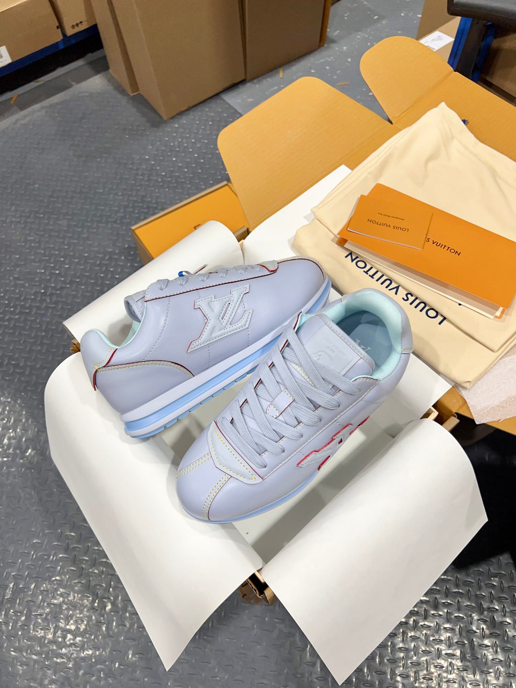 Light blue sneakers with side LV logo emblem, laces, and blue striped sole