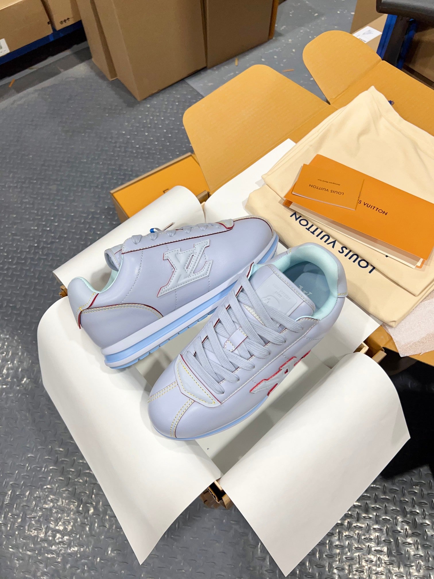 Light blue sneakers with side LV logo emblem, laces, and blue striped sole