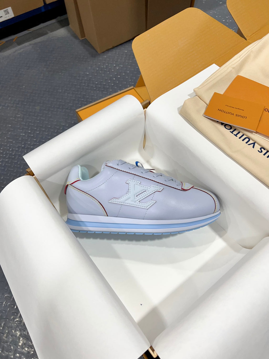 Single light blue sneaker in box with lace-up front and blue striped sole