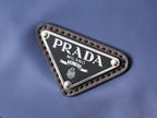 Prada logo patch on blue fabric bag, triangular metal-trim label