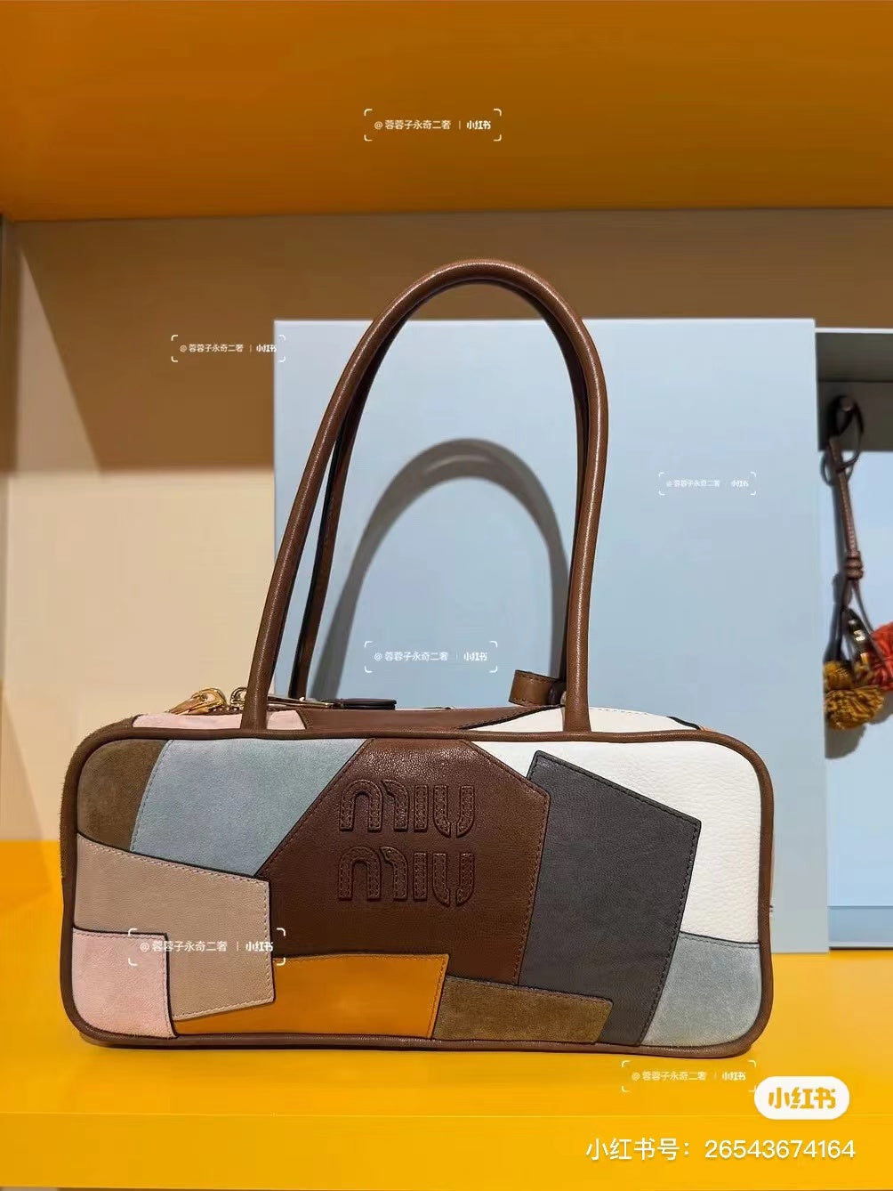 Patchwork leather bag on a display surface, brown handles, and square patch panels in cream, gray, and orange.
