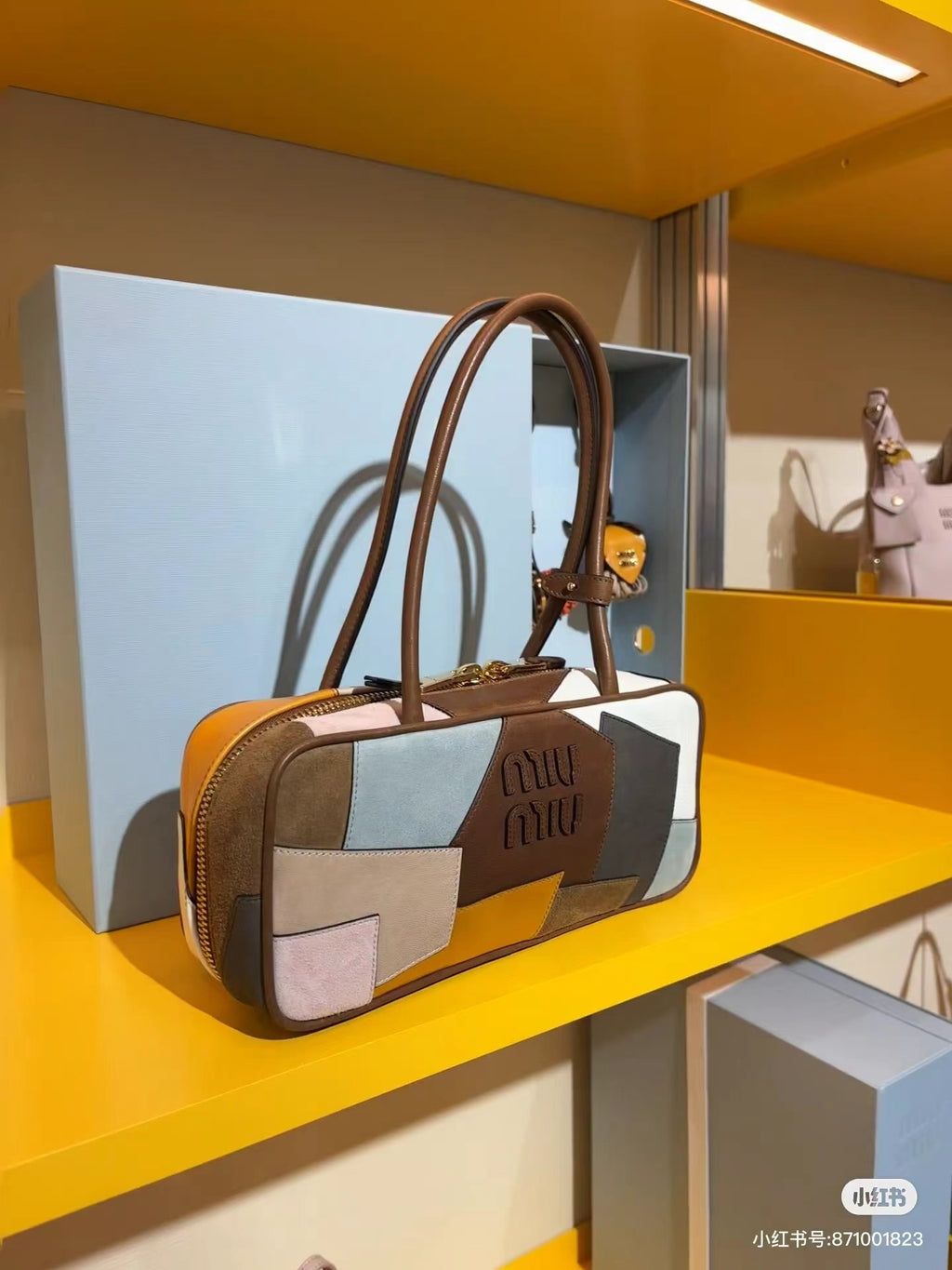 Patchwork leather bag with top handles and zip closure, featuring cream, gray, blue, and orange patch panels.
