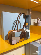 Patchwork leather bag with top handles and zip closure, featuring cream, gray, blue, and orange patch panels.