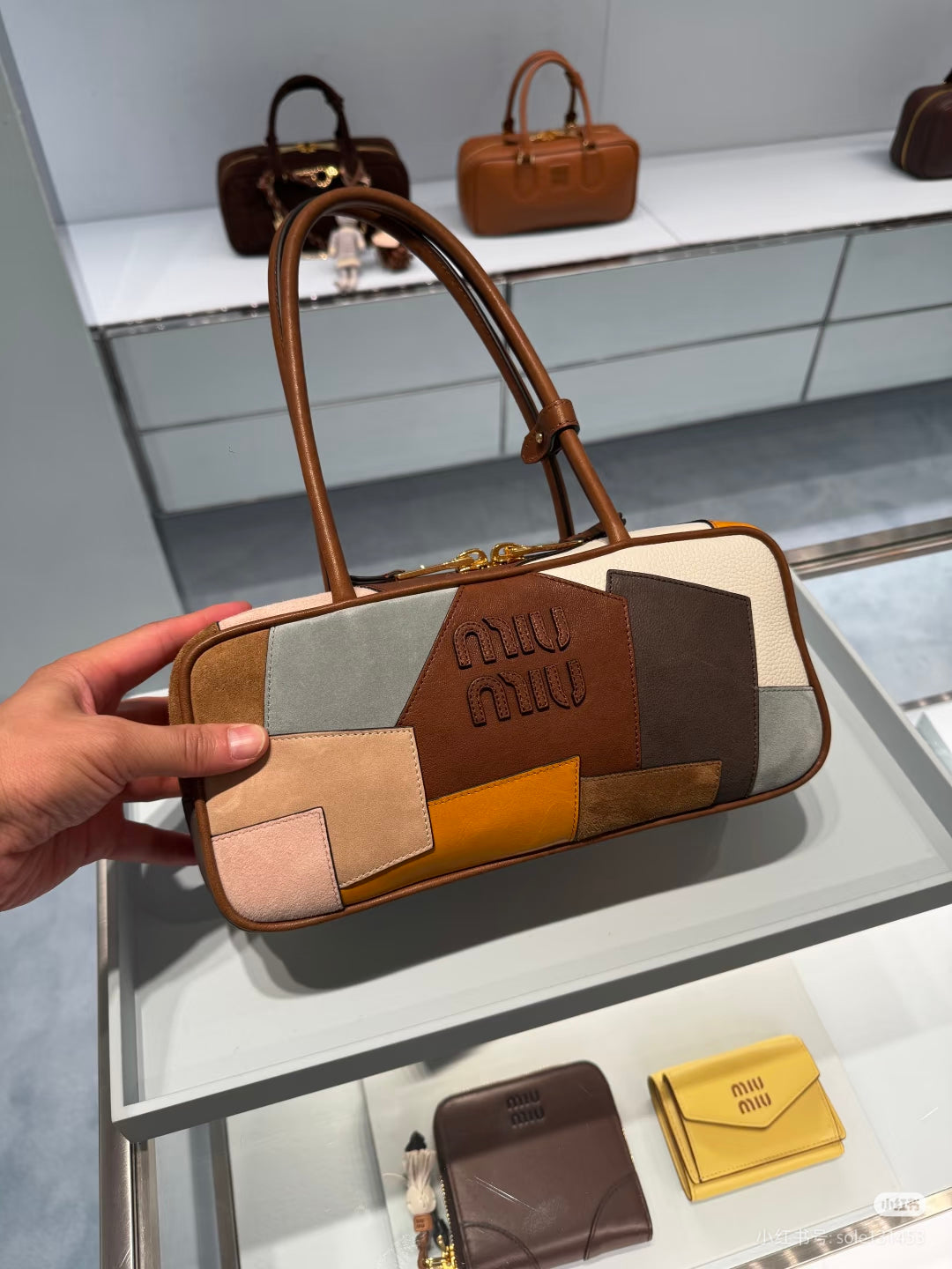 Patchwork leather bag held up, brown top handles, multicolor blocks, and embossed logo on center patch.