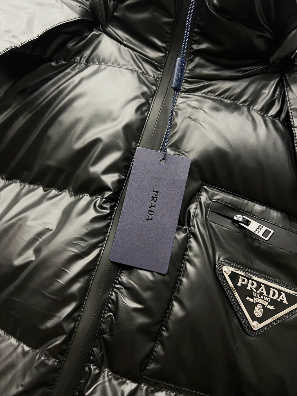 Black long puffer jacket detail with hanging tag and Prada logo patch