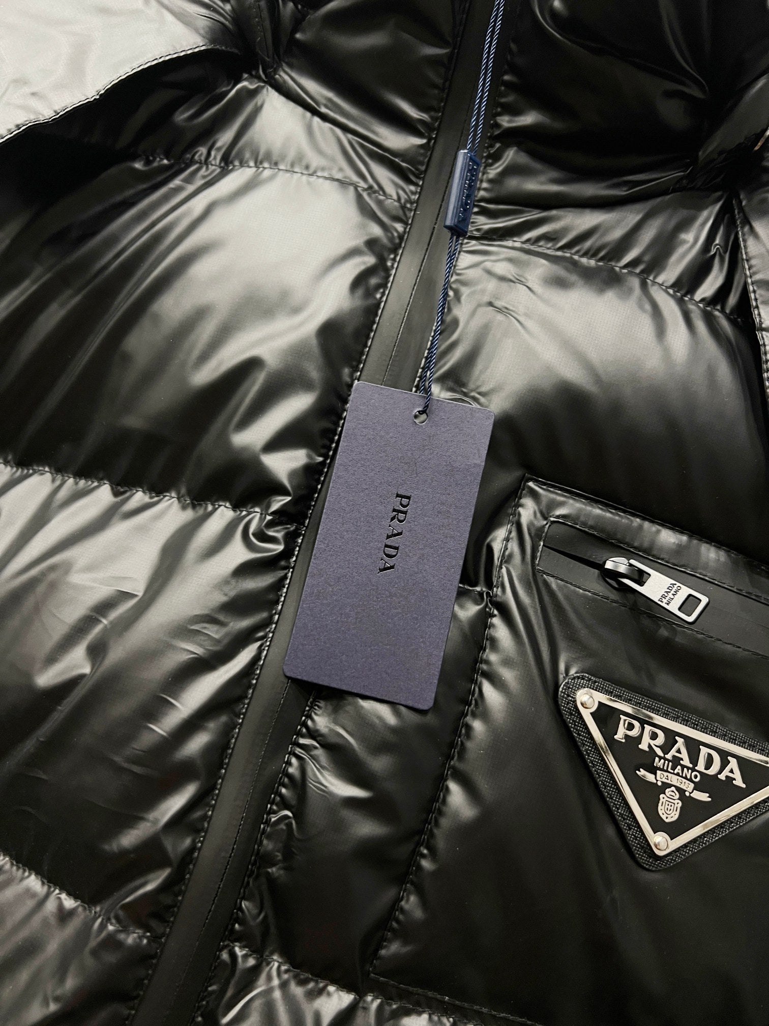 Black long puffer jacket detail with hanging tag and Prada logo patch