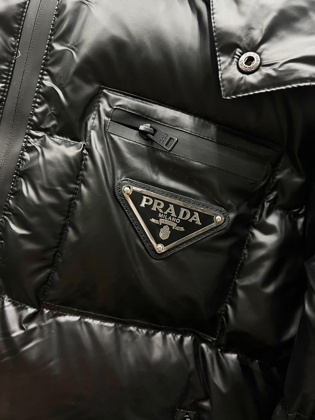 Black long puffer jacket chest pocket with Prada logo patch and snap button