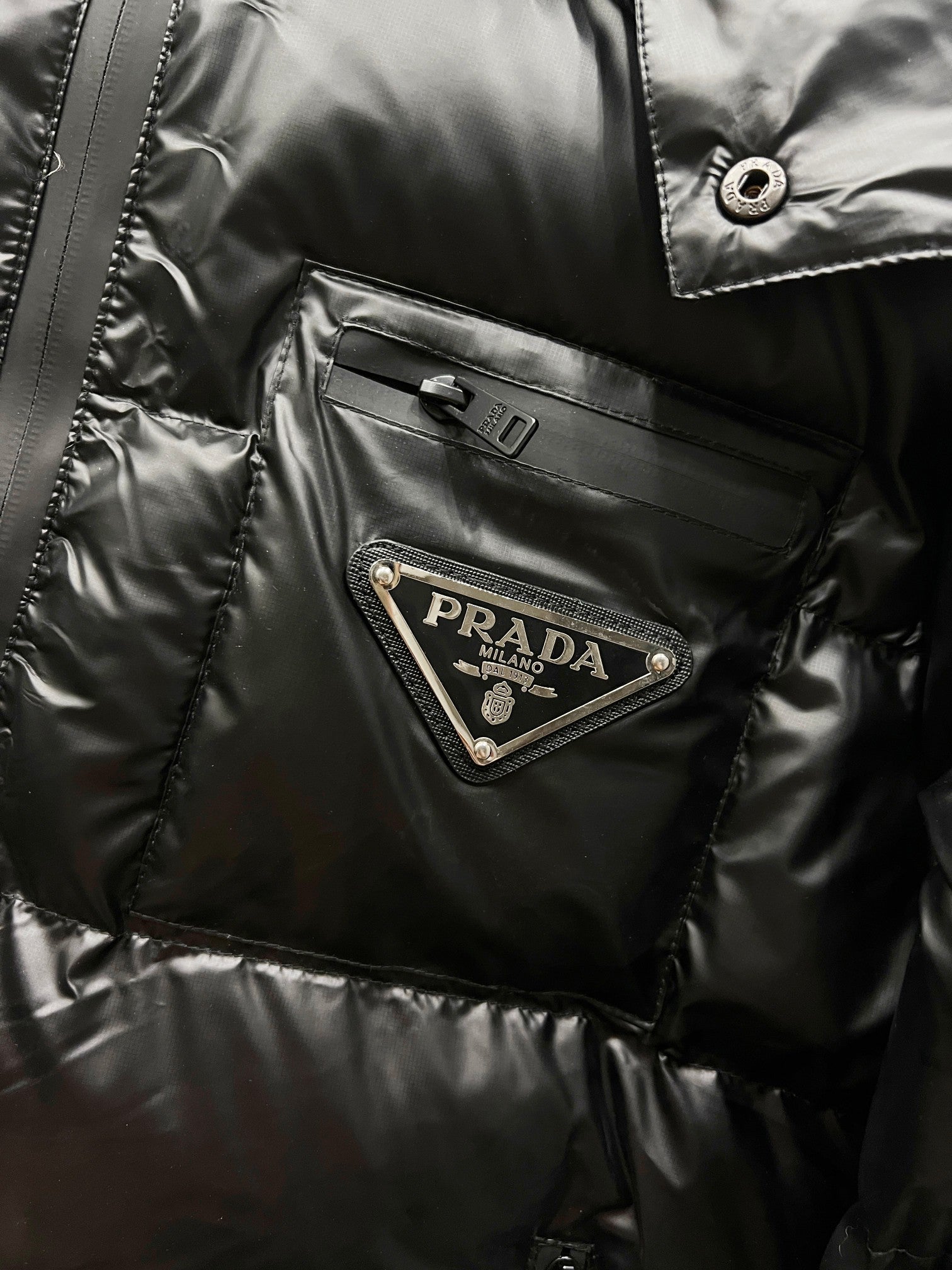 Black long puffer jacket chest pocket with Prada logo patch and snap button