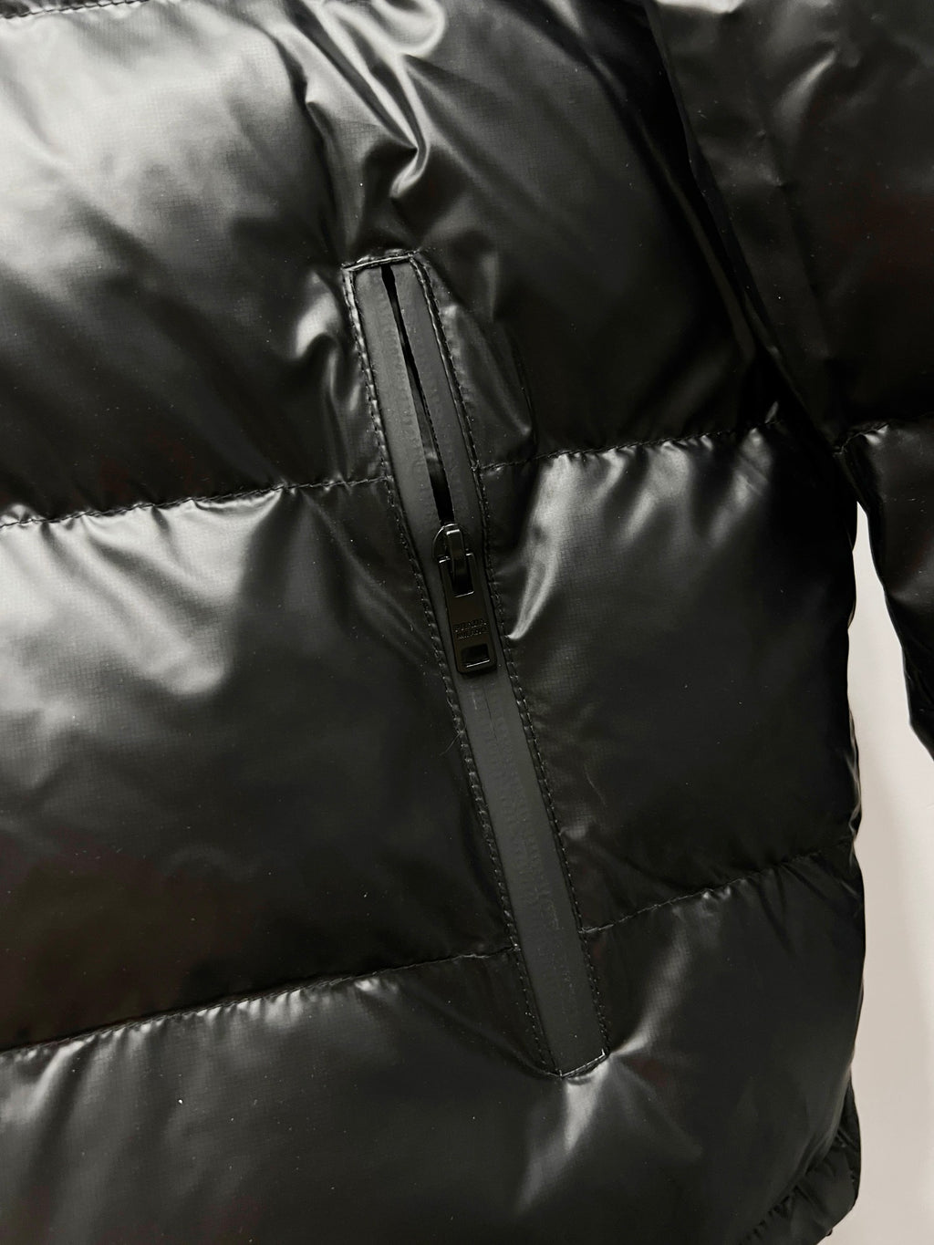 Black long puffer jacket side view with zip seam and quilted panels