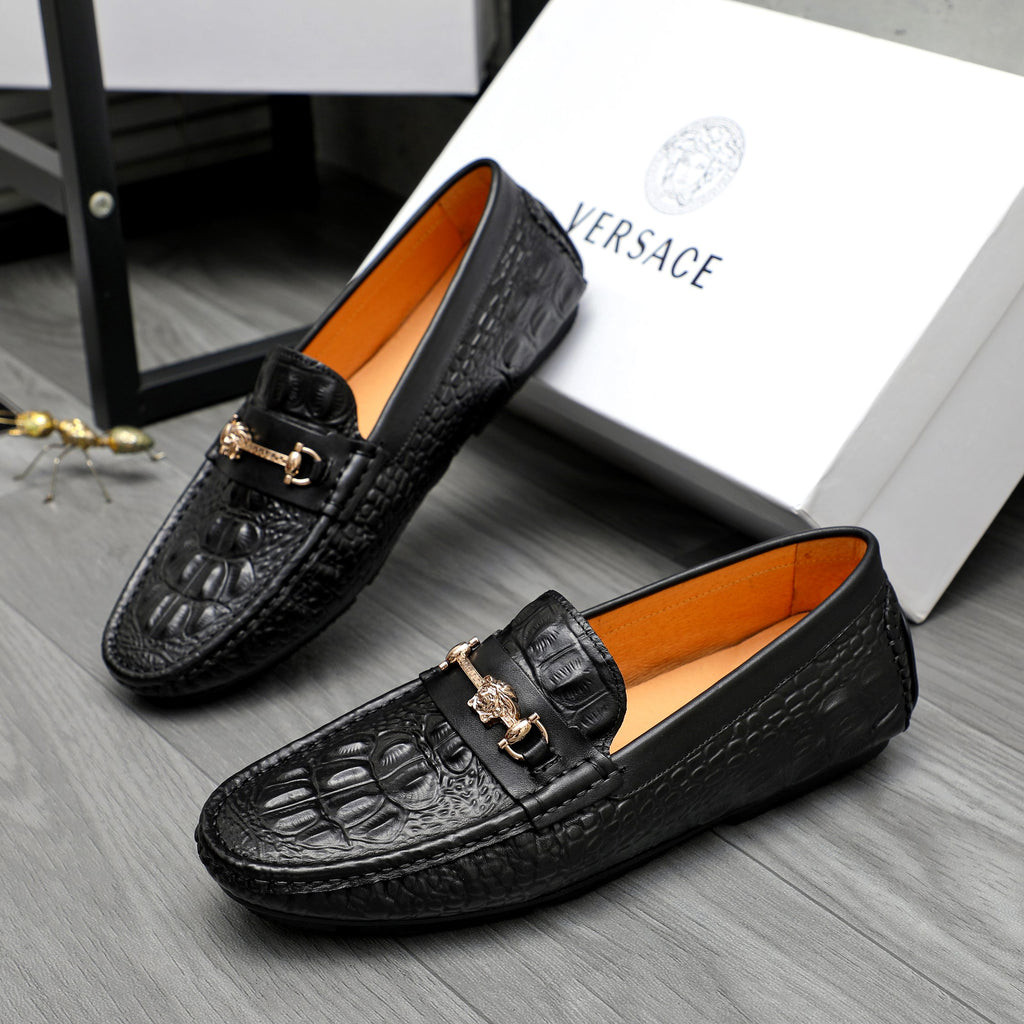 Black embossed leather loafers with gold-tone strap buckle and tan interior lining.