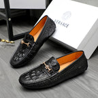 Black embossed leather loafers with gold-tone strap buckle and tan interior lining.