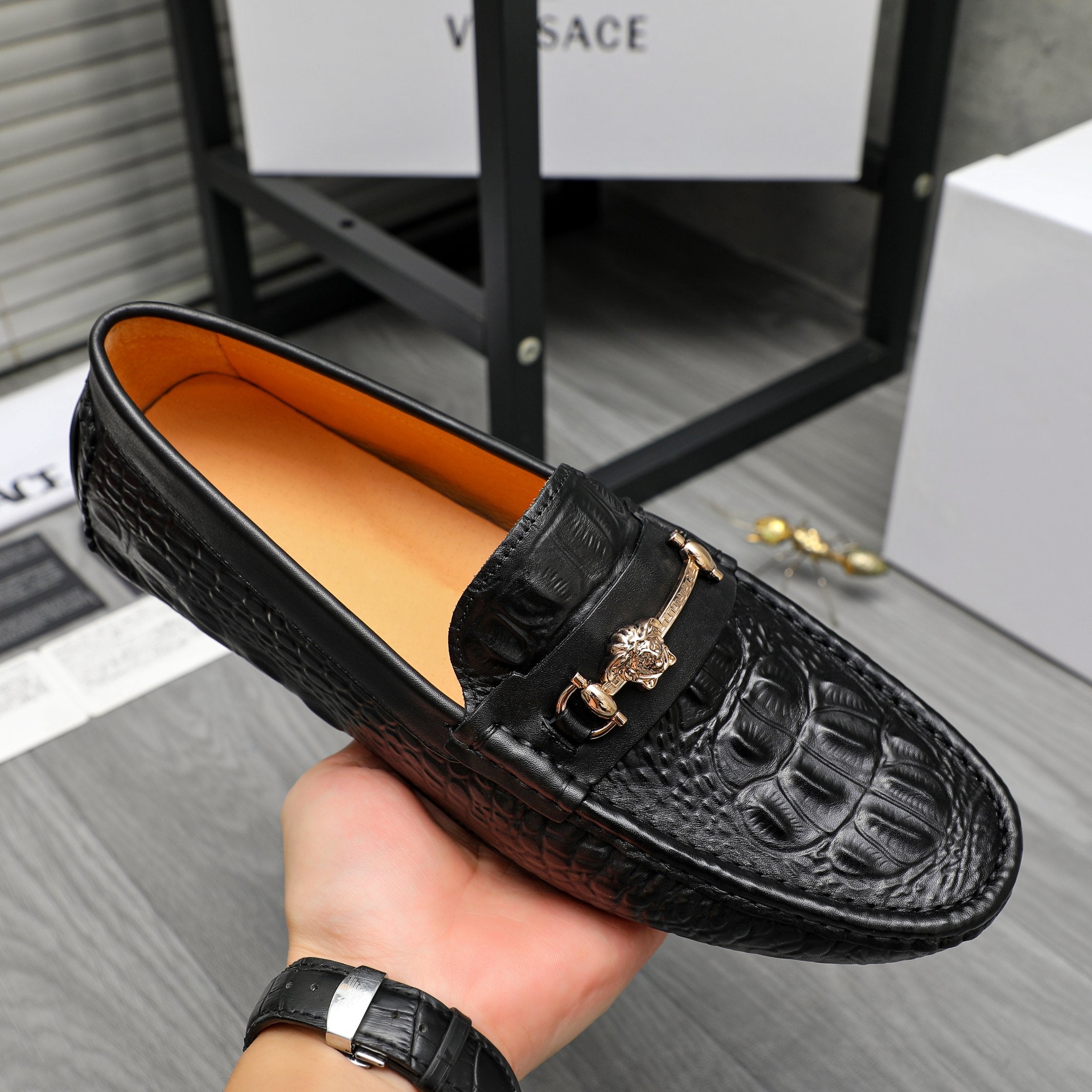Black embossed leather loafer with gold-tone buckle detail and tan-lined interior.